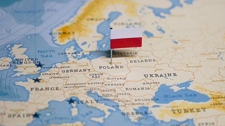 Zdjęcie zbliżenia na mapę Europy z wbitą w środku terytorium Polski małej flagi biało-czerwonej.